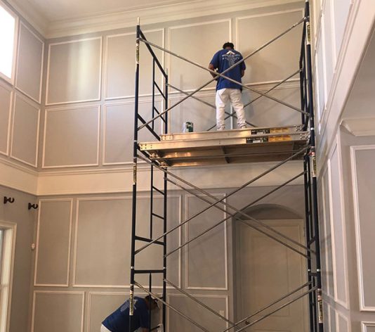 paint contractor on ladder painting the interior of home